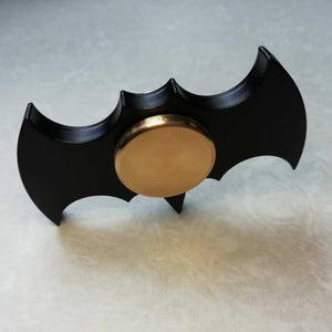 Black and gold fidget spinner shaped like a bat emblem on a light gray background