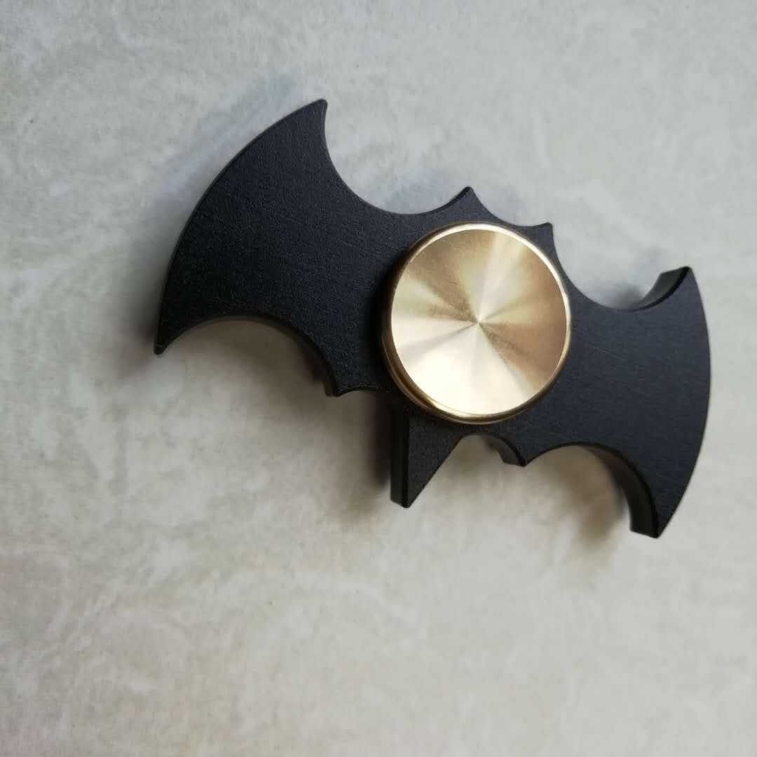 Black bat-shaped fidget spinner with a gold center on a light gray background