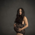 Pregnant woman wearing a black lace bodysuit against a dark background