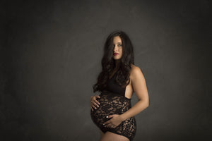 Pregnant woman wearing a black lace bodysuit against a dark background