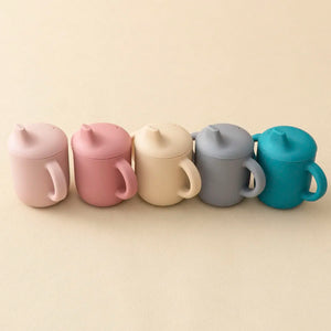 Five colorful sippy cups lined up on a beige background