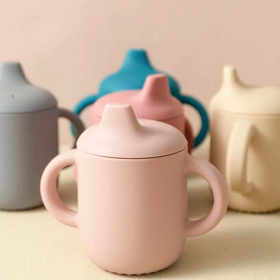 Pink ceramic mug with a lid on a beige surface with other ceramic items in the background.