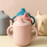 Pink ceramic mug with a lid on a beige surface with other ceramic items in the background.
