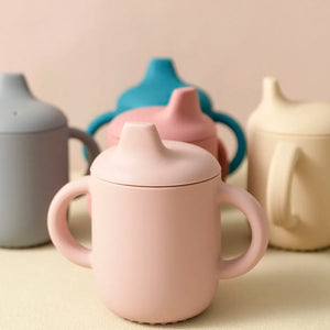 Pink ceramic mug with a lid on a beige surface with other ceramic items in the background.
