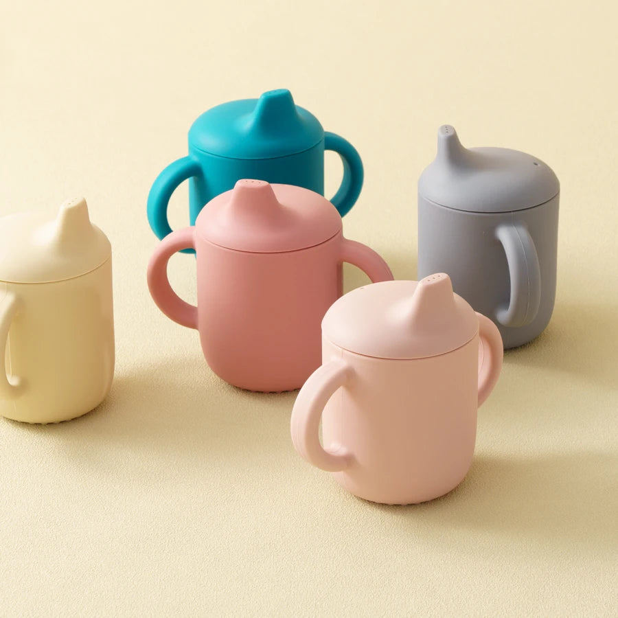Set of colorful sippy cups on a beige background