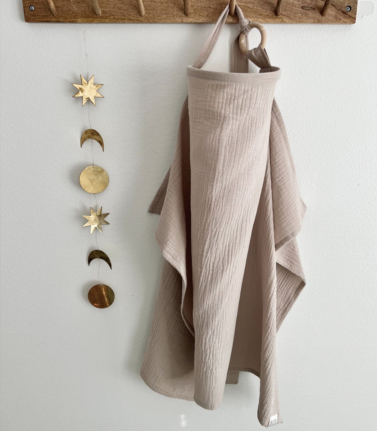 Beige fabric hanging from a wooden hook with decorative metal phases of the moon on a white wall.