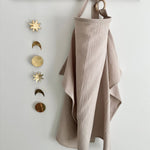 Beige fabric hanging from a wooden hook with decorative metal phases of the moon on a white wall.