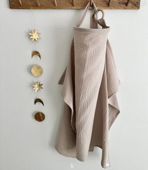 Beige fabric hanging from a wooden hook with decorative metal phases of the moon on a white wall.