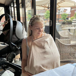 Woman sitting at a table with a baby in a sling in an outdoor setting