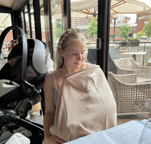 Woman sitting at a table with a baby in a sling in an outdoor setting