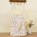 Floral dress hanging on a rack with a vase of flowers on a wooden floor.