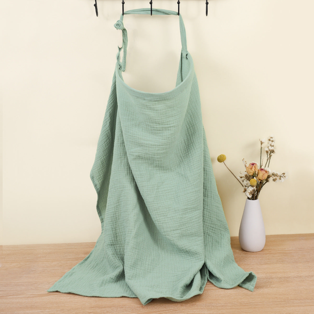 Green apron on a mannequin against a beige wall with a vase of flowers.