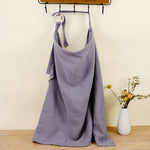Purple dress hanging on a rack with a vase of flowers on a wooden floor.
