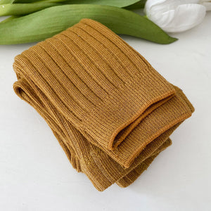 Folded brown towel on a white surface with green leaves in the background