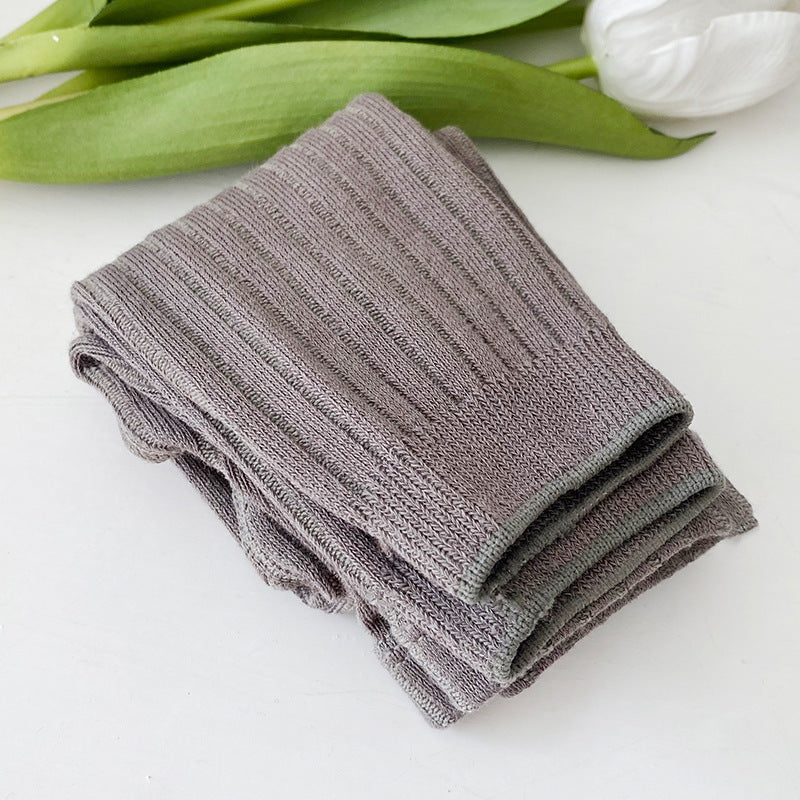 Folded gray towel on a white surface with green leaves and a white flower in the background