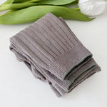 Folded gray towel on a white surface with green leaves and a white flower in the background