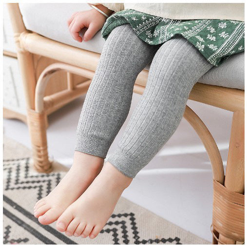 Child's legs wearing gray leggings sitting on a wooden chair.