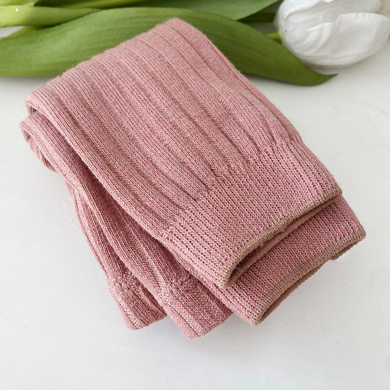 Folded pink knitted blanket on a white surface with green leaves in the background
