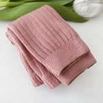 Folded pink knitted blanket on a white surface with green leaves in the background