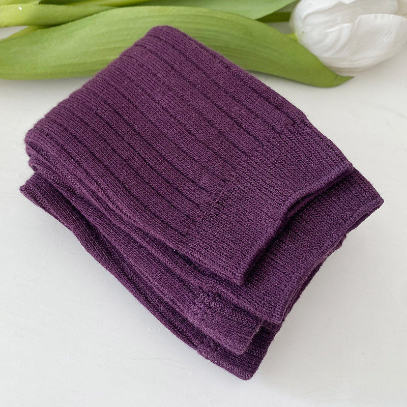 Folded purple towel on a white surface with green leaves in the background