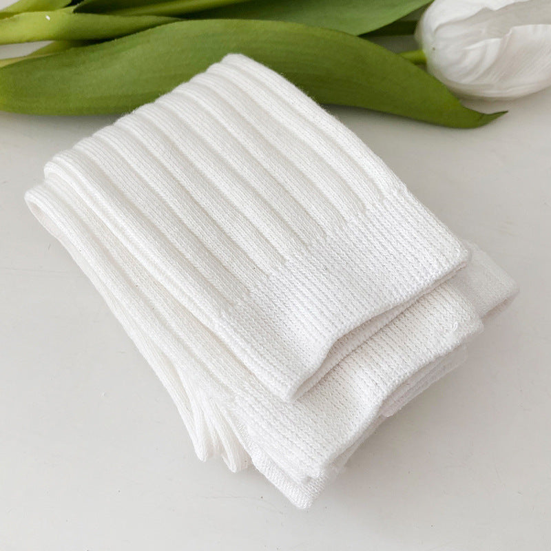 Stack of white socks on a light surface with green leaves in the background