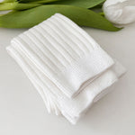 Stack of white socks on a light surface with green leaves in the background
