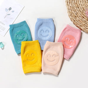 Set of colorful knitted knee pads with smiley face designs on a light background.