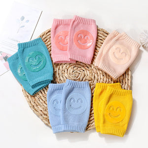 Set of colorful baby knee pads with smiley face designs on a woven mat.