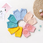 Colorful baby knee pads with smiley face designs arranged in a circle on a light background.