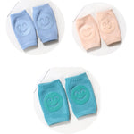 Set of baby knee pads in blue, pink, and turquoise with smiley face designs on a white background.