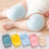 Baby wearing light blue knee pads with smiley face design on a wooden floor.