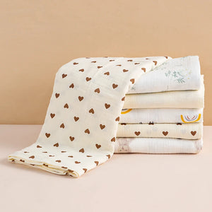 Stack of folded baby blankets with heart patterns on a beige background