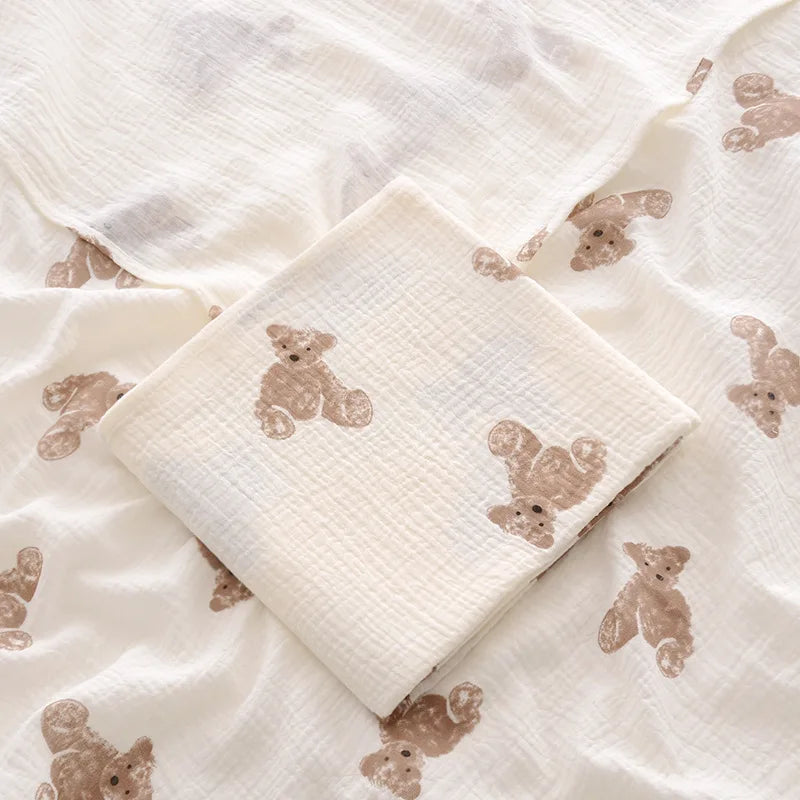 White baby blanket with brown teddy bear patterns on a matching white pillow.