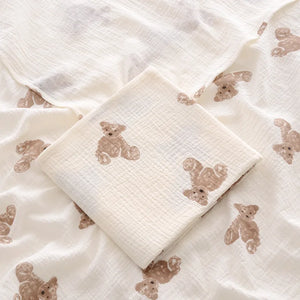 White baby blanket with brown teddy bear patterns on a matching white pillow.