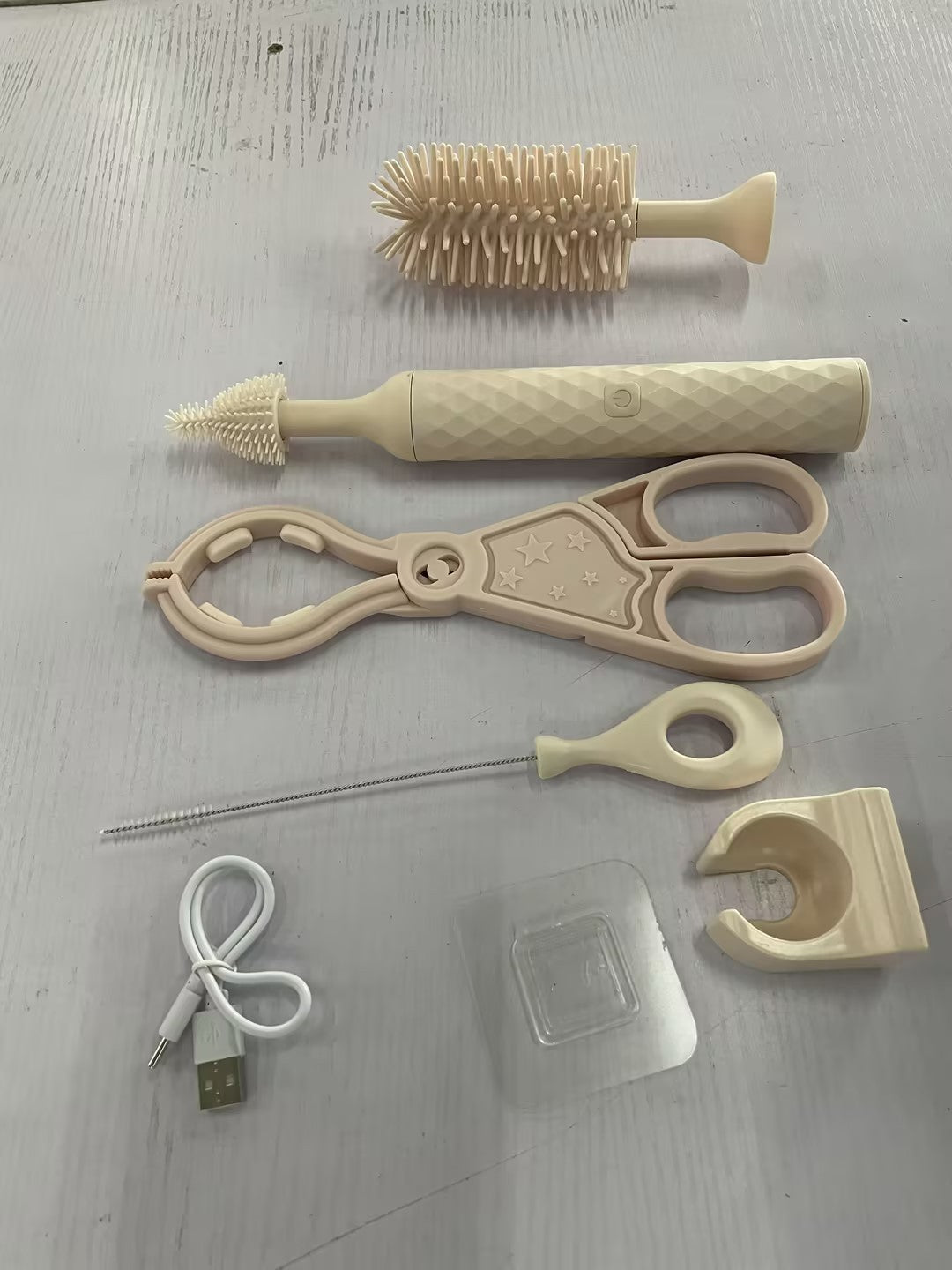 Collection of baby care items including brushes, scissors, and a USB cable on a light gray surface.
