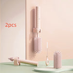Two pink hairbrushes with a holder on a light green surface and pastel pink background.