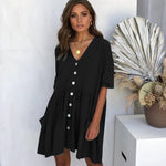 Woman wearing a black dress with white buttons in a minimalistic setting.