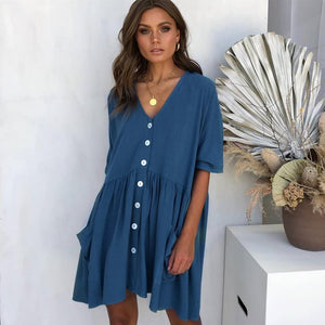 Woman wearing a blue dress with white buttons in a minimalistic setting.