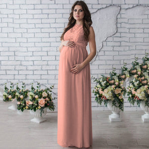 Woman in a long pink dress standing in front of a white brick wall with floral arrangements.