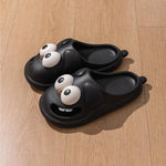 Black slippers with googly eyes on a wooden floor