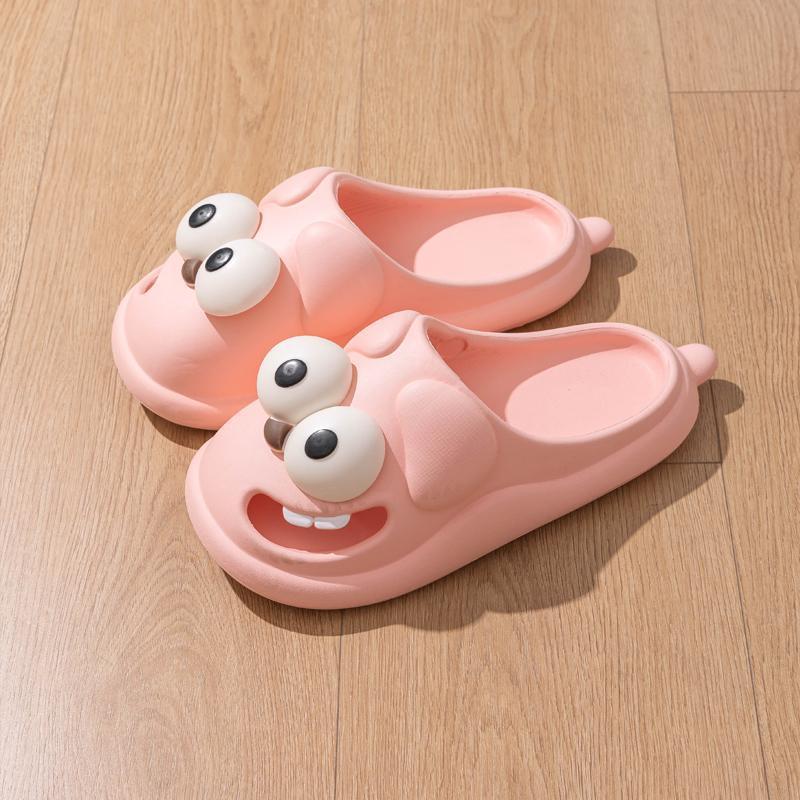 Pink cartoon-style slippers with googly eyes on a wooden floor