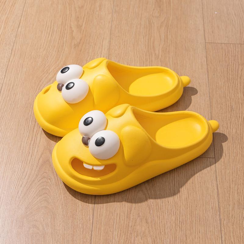 Pair of yellow slippers with cartoonish face design on a wooden floor.