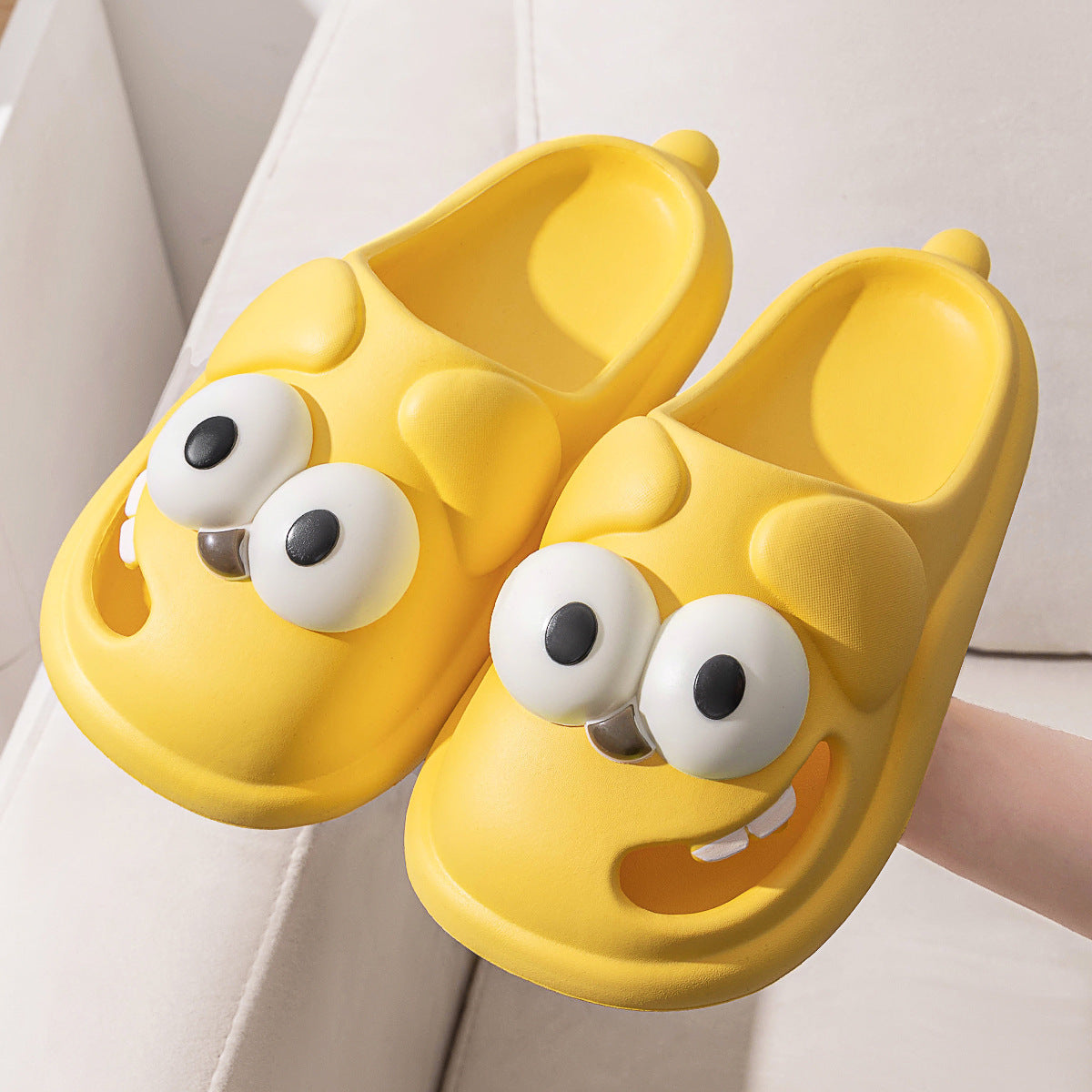 Yellow cartoon-style slippers with googly eyes and a smile on a light background