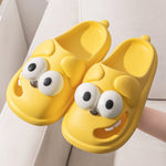 Yellow cartoon-style slippers with googly eyes and a smile on a light background