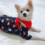 Small white dog wearing a festive pajama with Christmas patterns on a white blanket.
