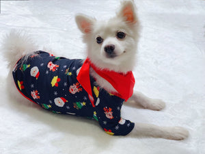 Small white dog wearing a festive pajama with Christmas patterns on a white blanket.