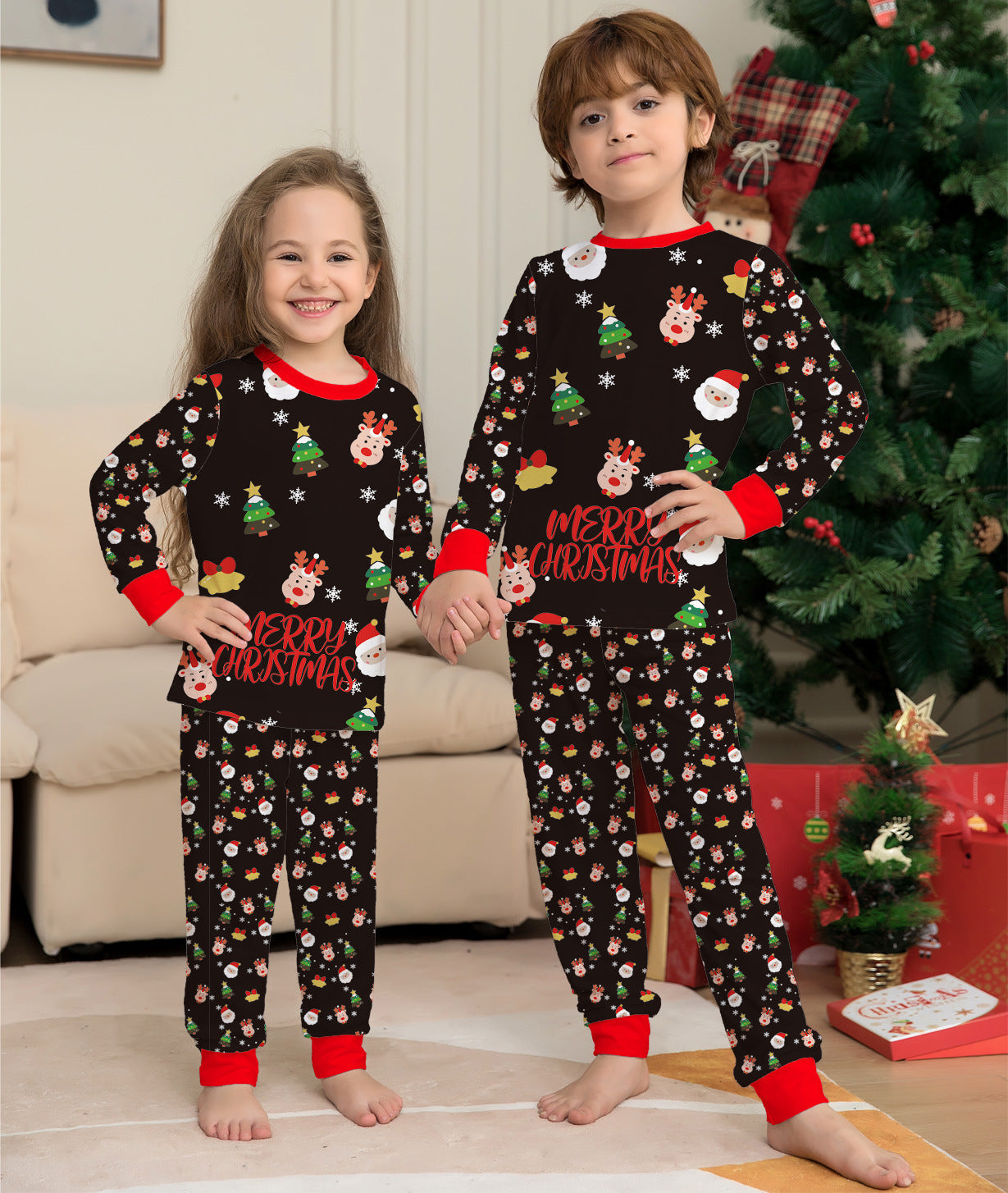 Two children wearing Christmas-themed pajamas in a living room with a decorated tree.