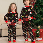 Two children wearing Christmas-themed pajamas in a living room with a decorated tree.