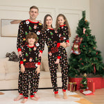 Family of four wearing matching Christmas pajamas in a living room with a decorated tree.