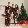Family of four wearing matching Christmas pajamas in a living room with a decorated tree.